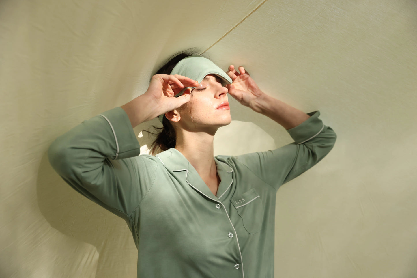 Woman wearing a sage green bamboo pajama set and matching sleep mask by GYS, bathed in soft light, showcasing breathable, sustainable sleepwear made for calm and comfort.